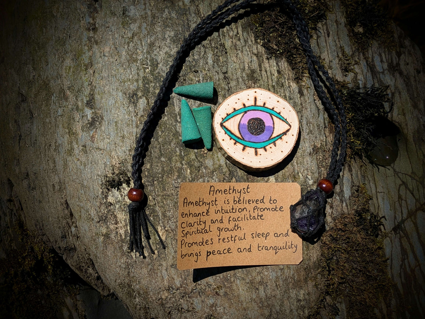 A picture of an ethically sourced Hematite crystal necklace, with incense and pyrography/ woodburning round