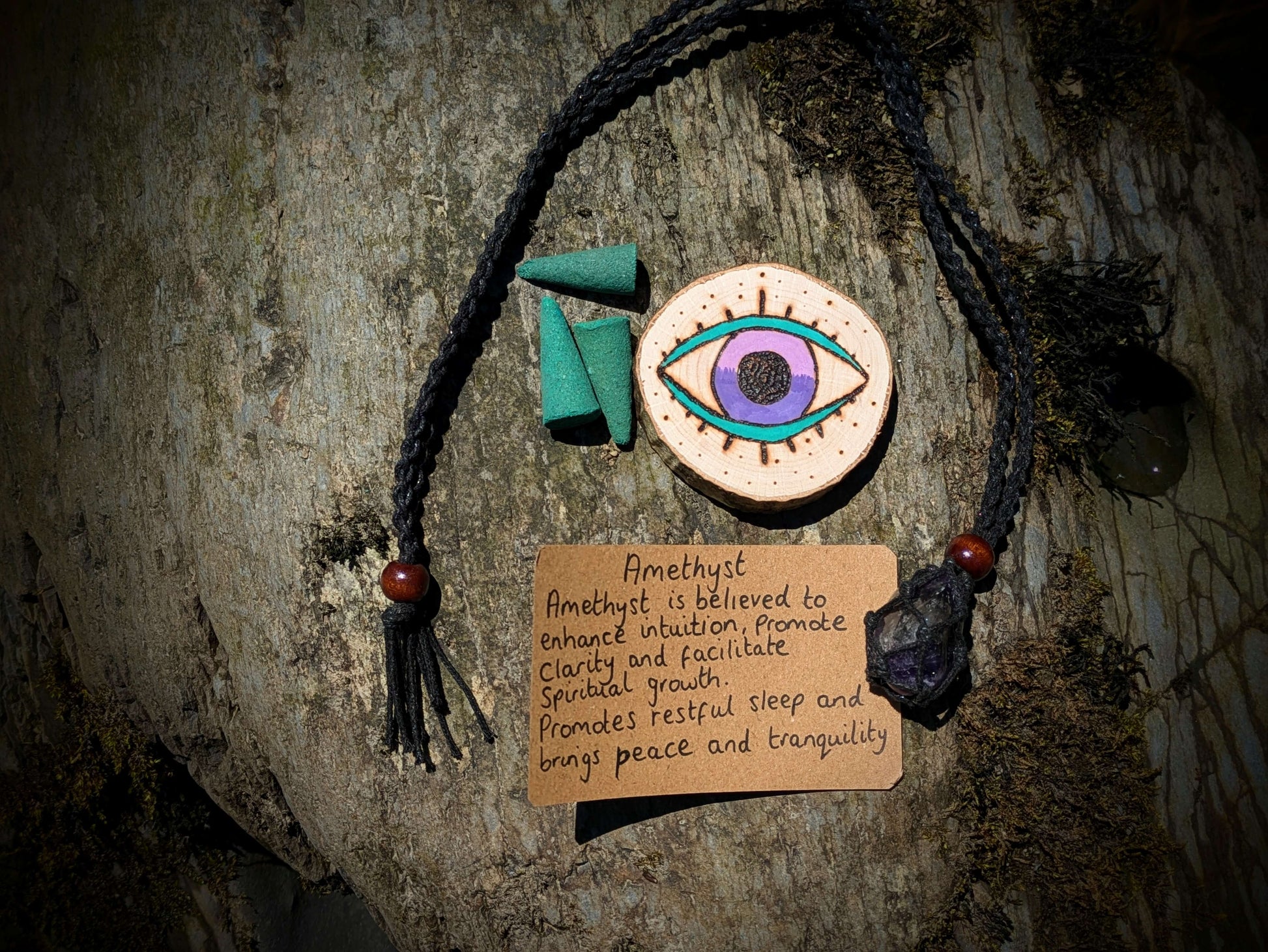 A picture of an ethically sourced Hematite crystal necklace, with incense and pyrography/ woodburning round