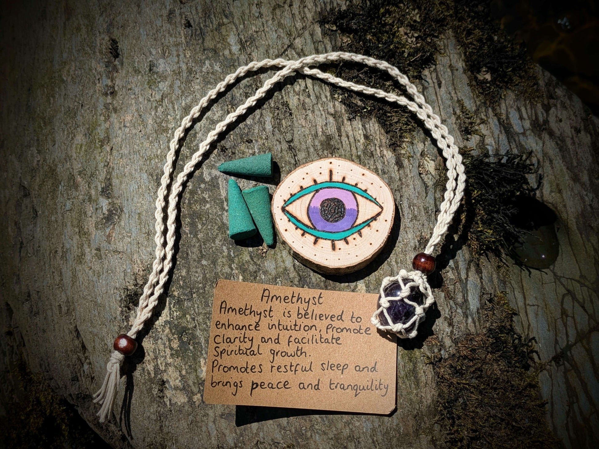 A picture of an ethically sourced Hematite crystal necklace, with incense and pyrography/ woodburning round