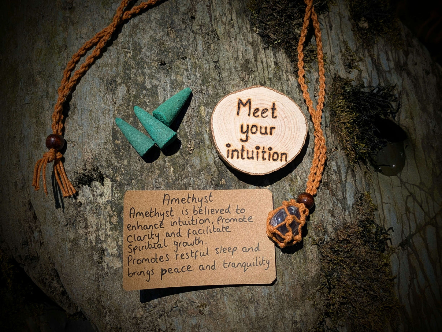 A picture of an ethically sourced Hematite crystal necklace, with incense and pyrography/ woodburning round
