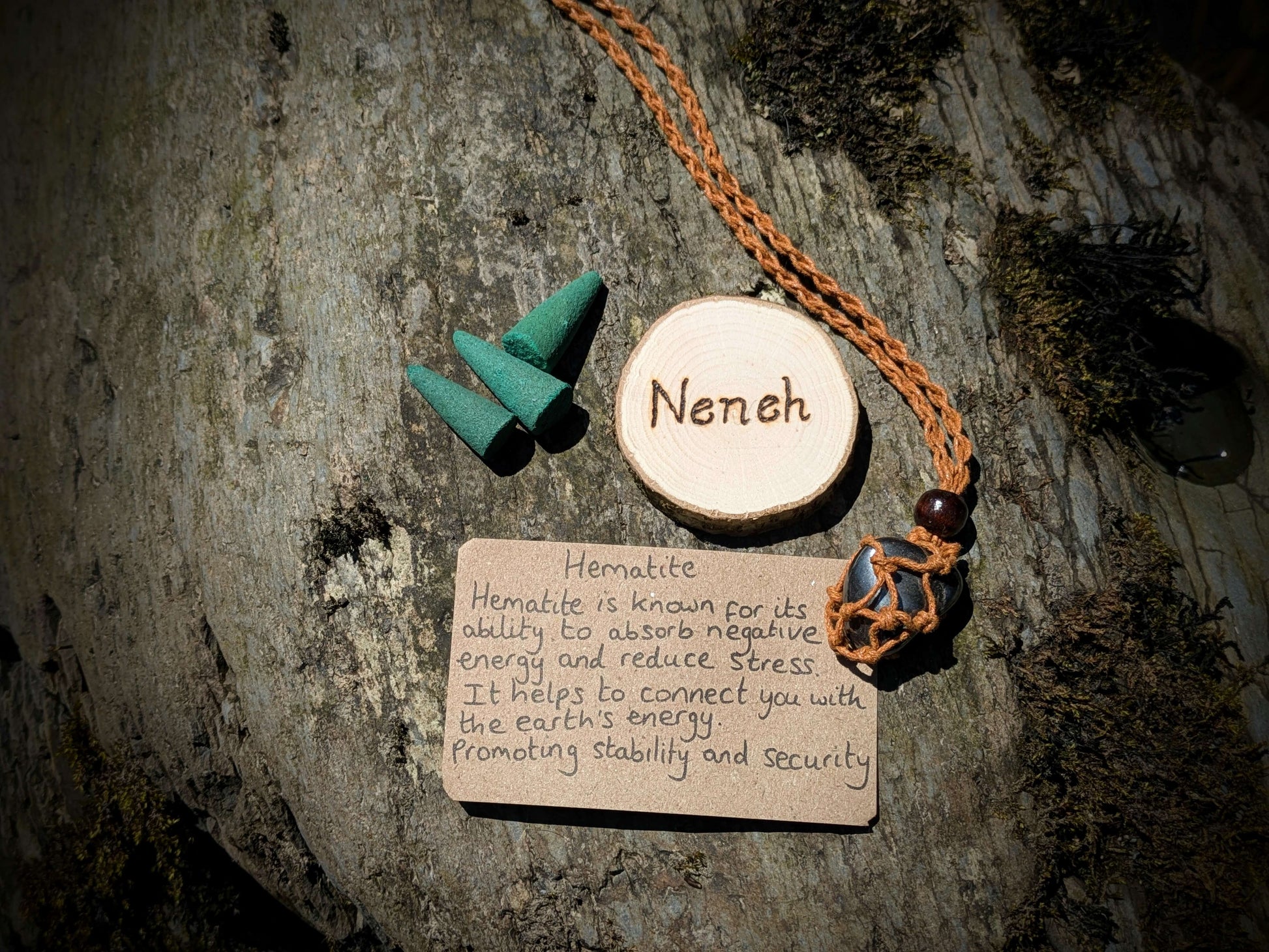 A picture of an ethically sourced Hematite crystal necklace, with incense and pyrography/ woodburning round