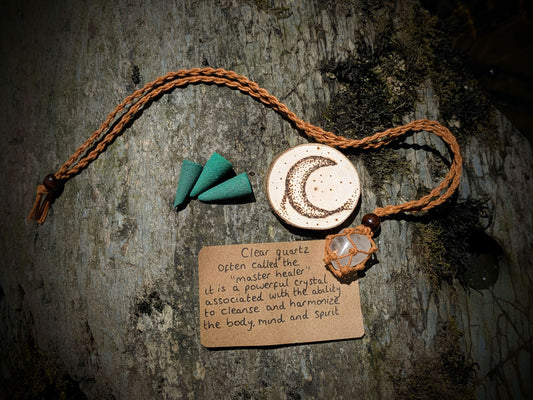A picture of an ethically sourced Clear Quartz crystal necklace, with incense and pyrography/ woodburning round