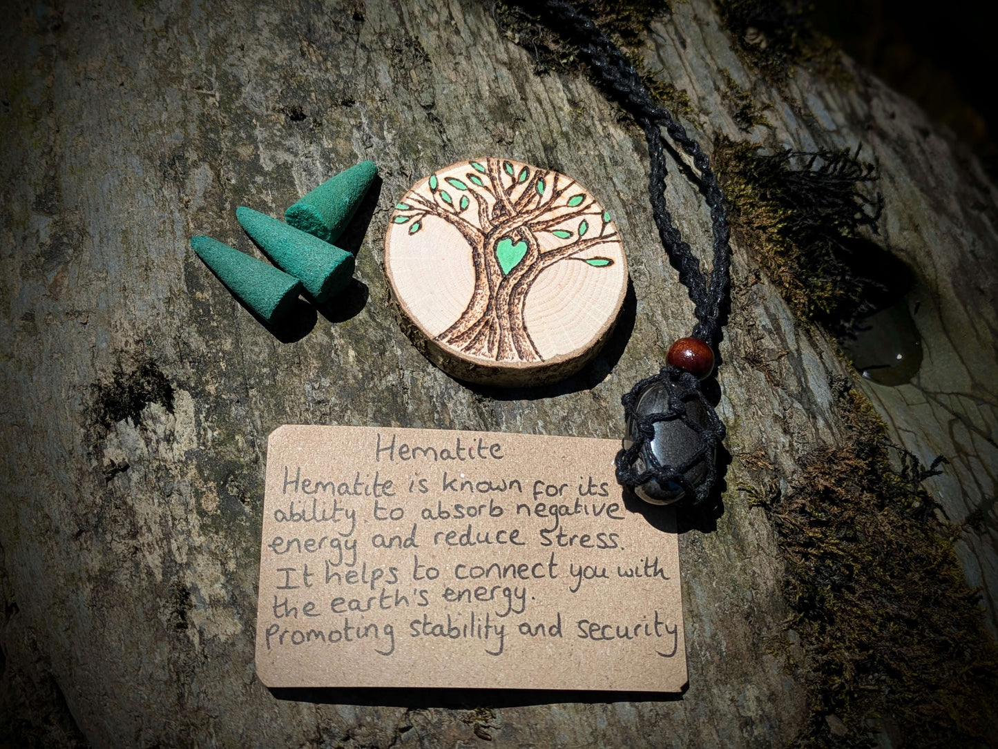 A picture of an ethically sourced Hematite crystal necklace, with incense and pyrography/ woodburning round