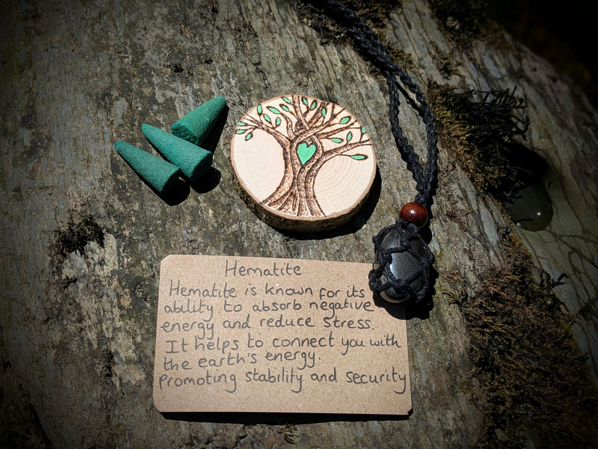 A picture of an ethically sourced Hematite crystal necklace, with incense and pyrography/ woodburning round