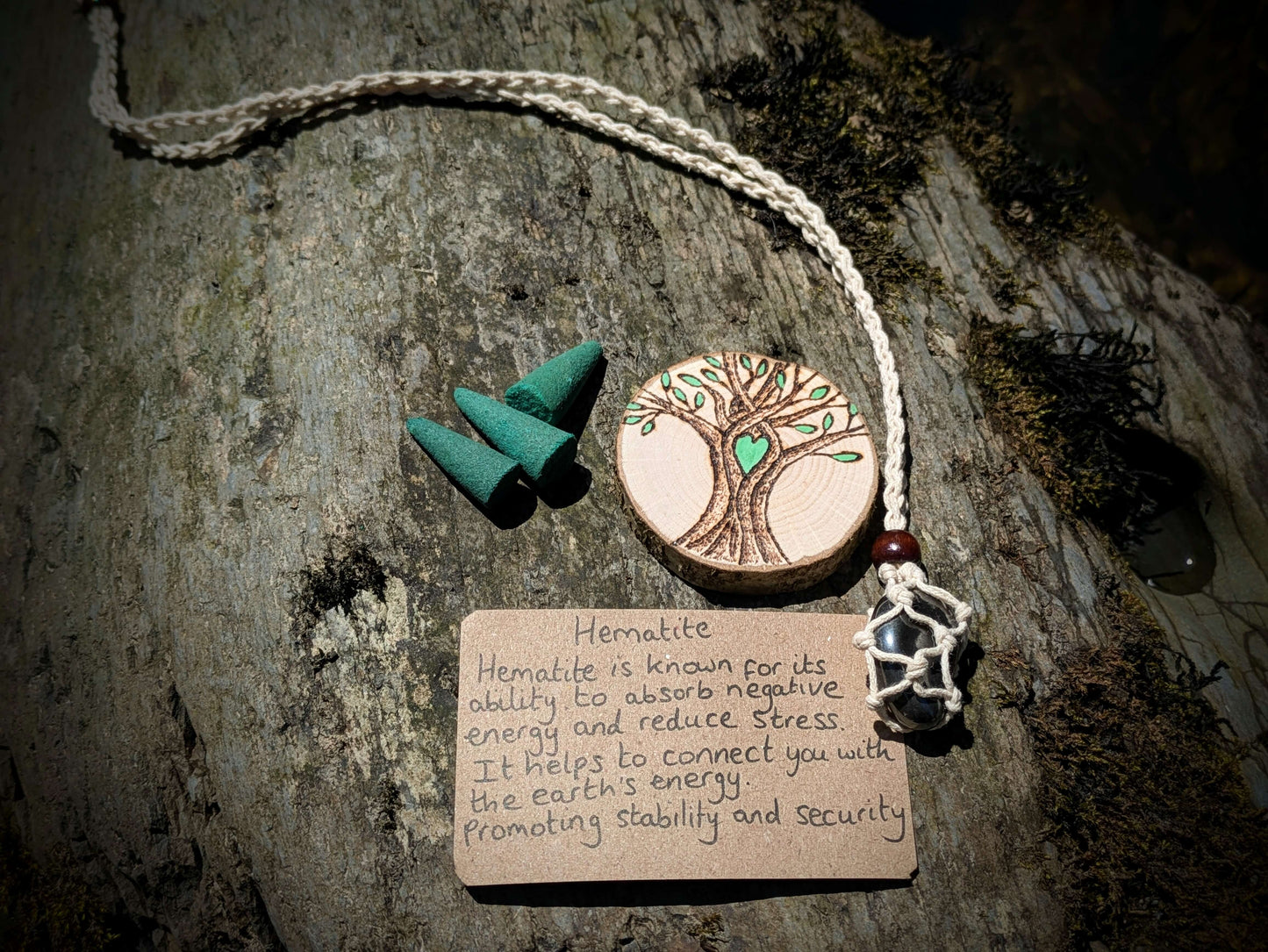 A picture of an ethically sourced Hematite crystal necklace, with incense and pyrography/ woodburning round