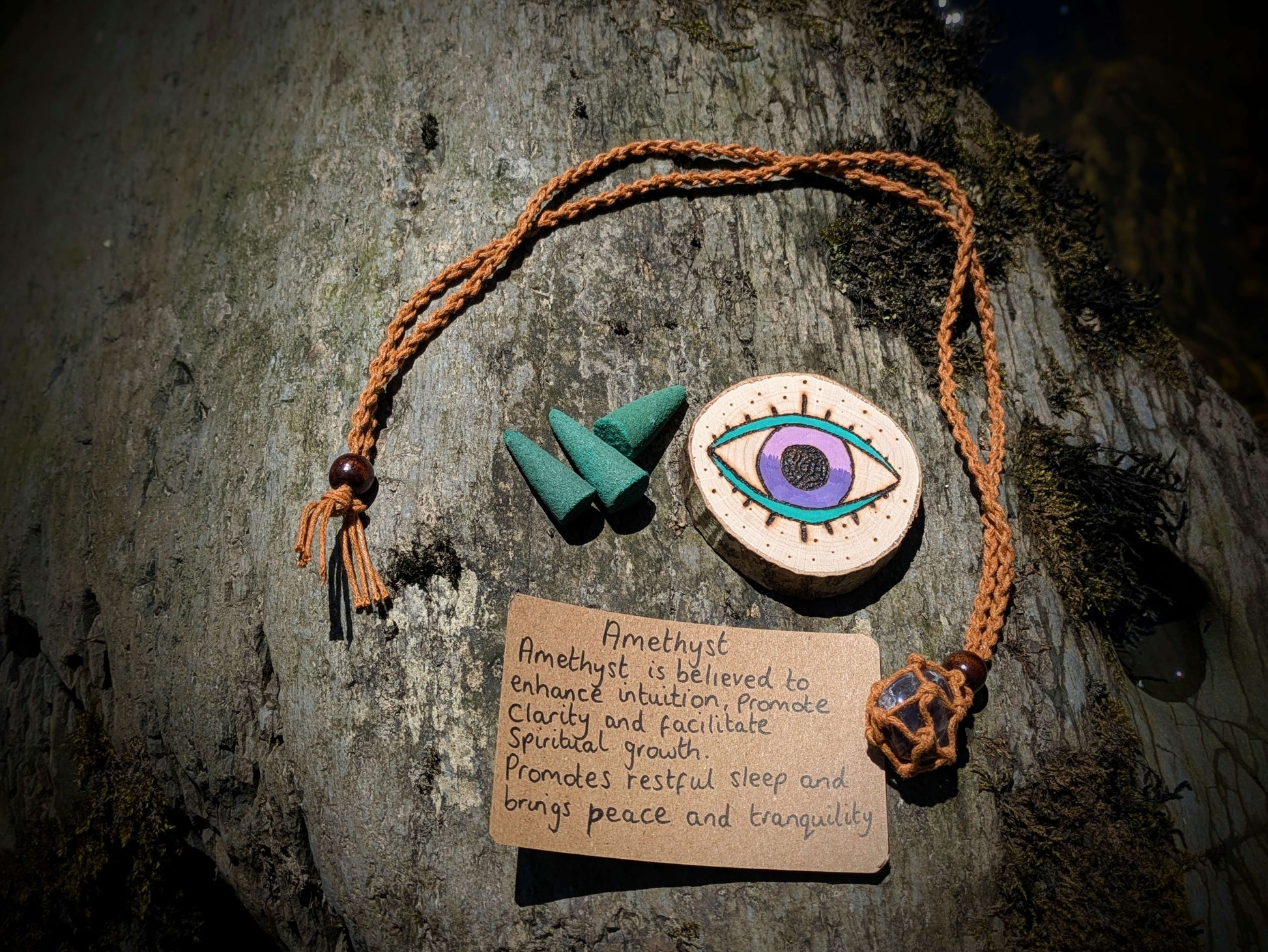 A picture of an ethically sourced Hematite crystal necklace, with incense and pyrography/ woodburning round