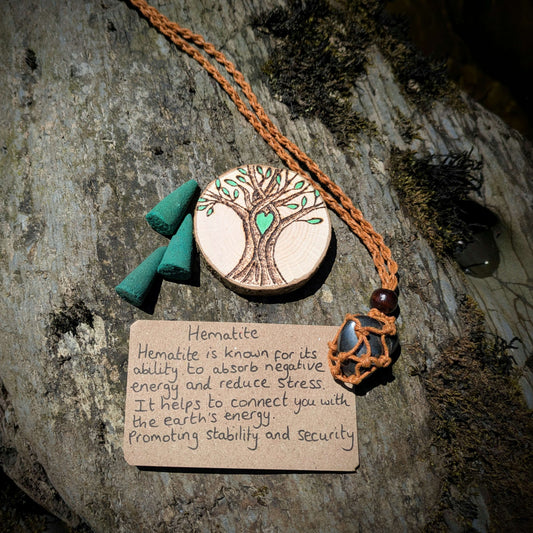 A picture of an ethically sourced Hematite crystal necklace, with incense and pyrography/ woodburning round
