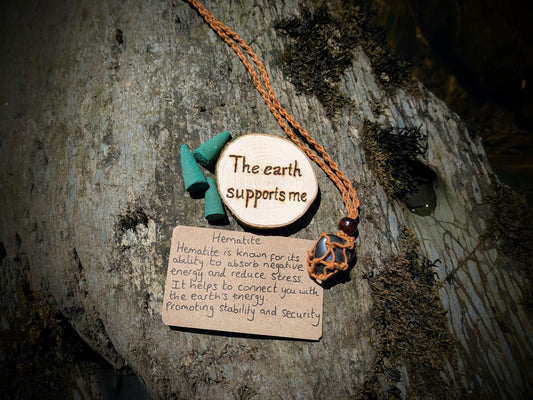 A picture of an ethically sourced Hematite crystal necklace, with incense and pyrography/ woodburning round
