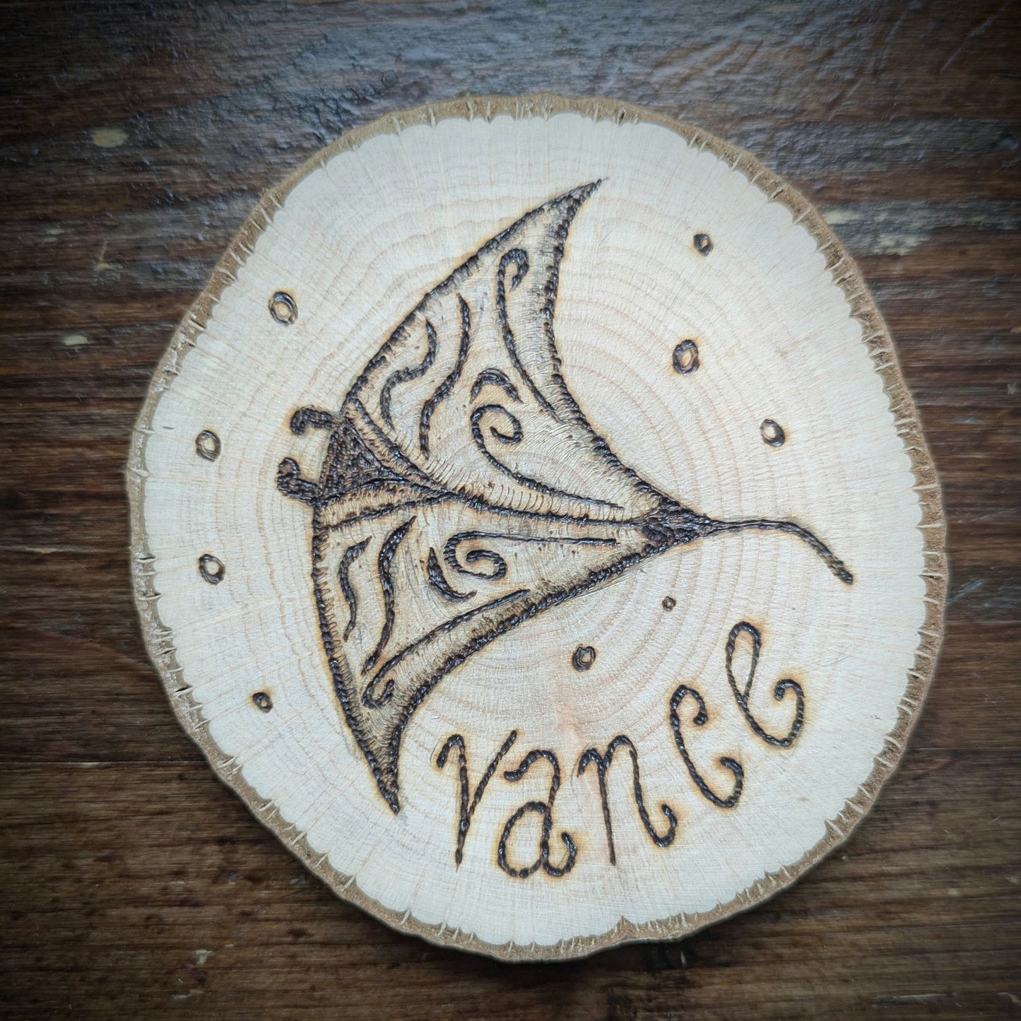 Wooden disc with manta ray design and 'vance' engraving on a wooden surface