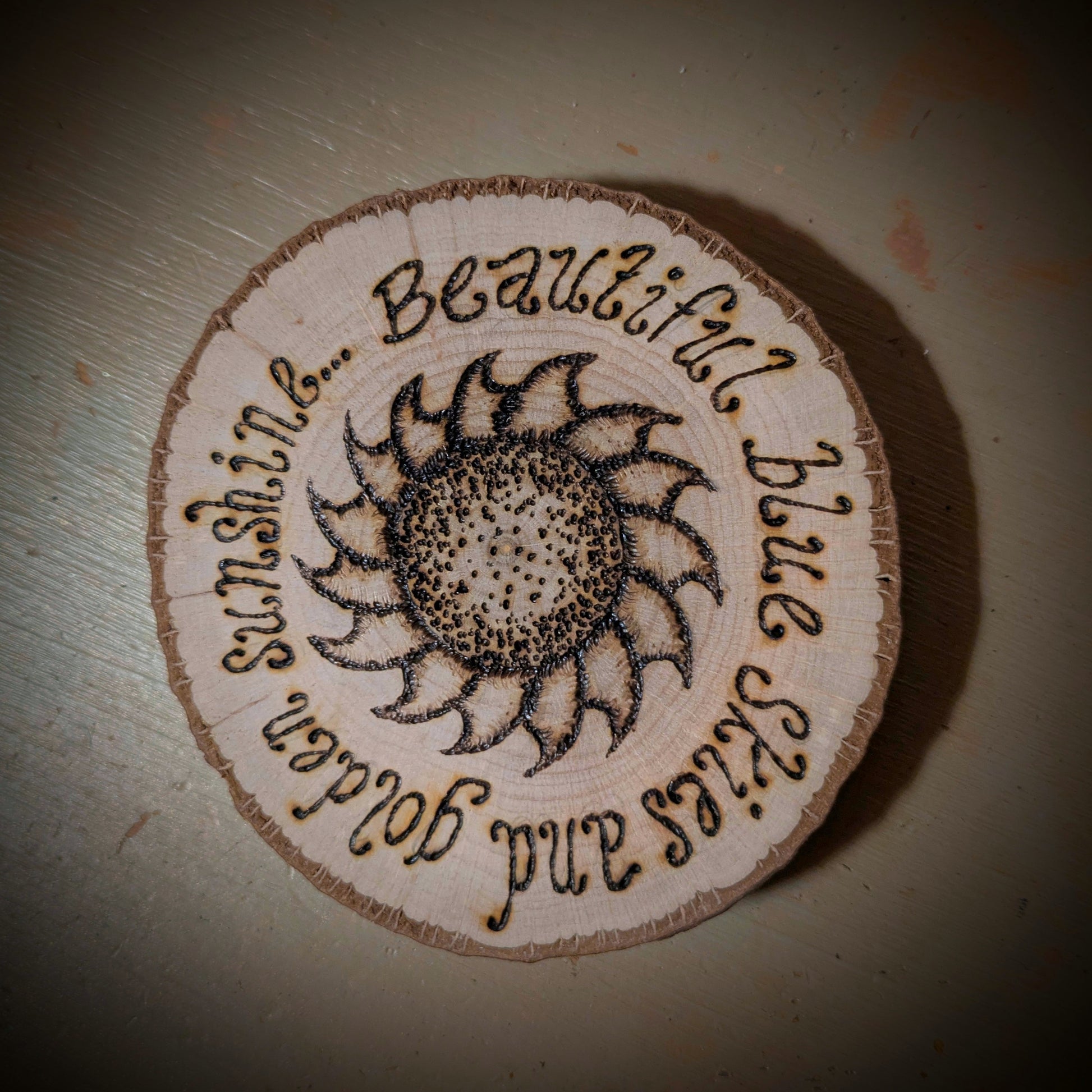 Circular wooden coaster with sunflower design and text on a plain background