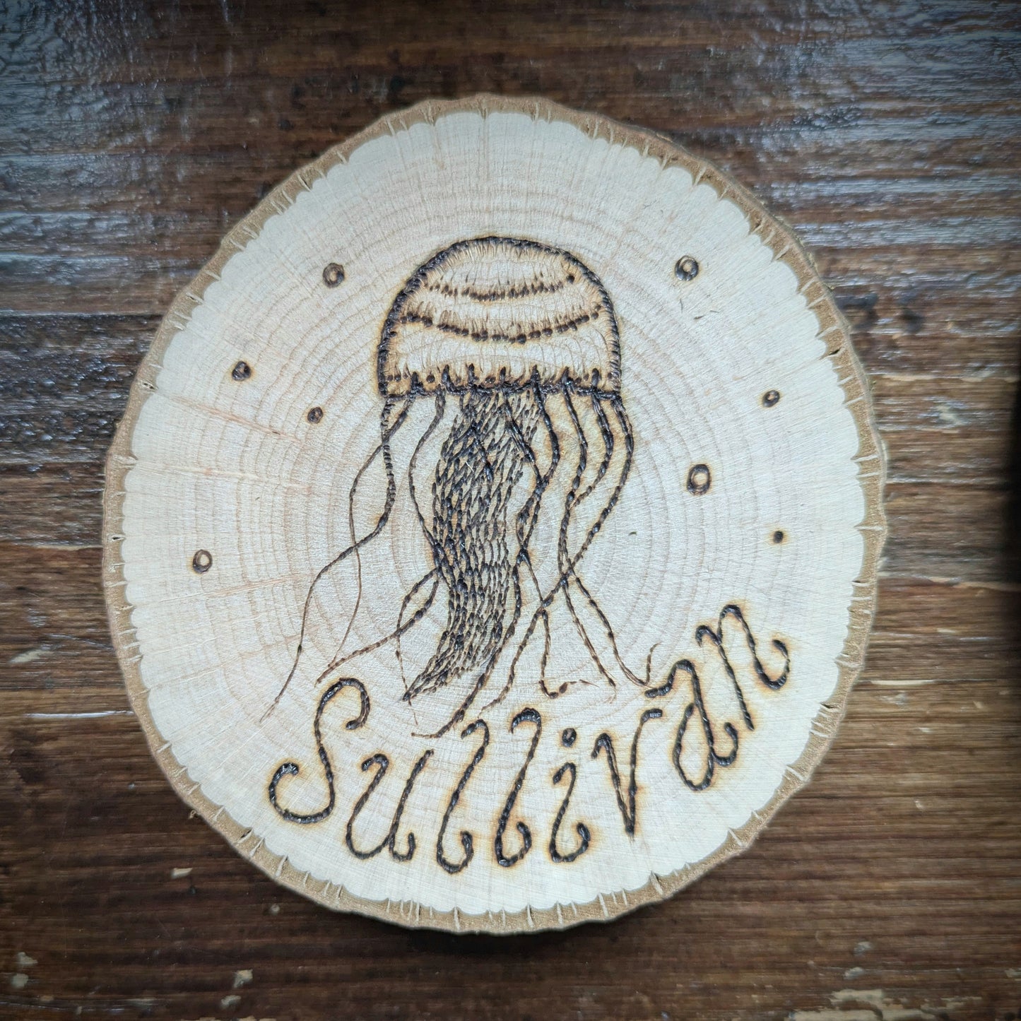 Wooden coaster with a jellyfish design and 'Sullivan' engraving on a wooden surface