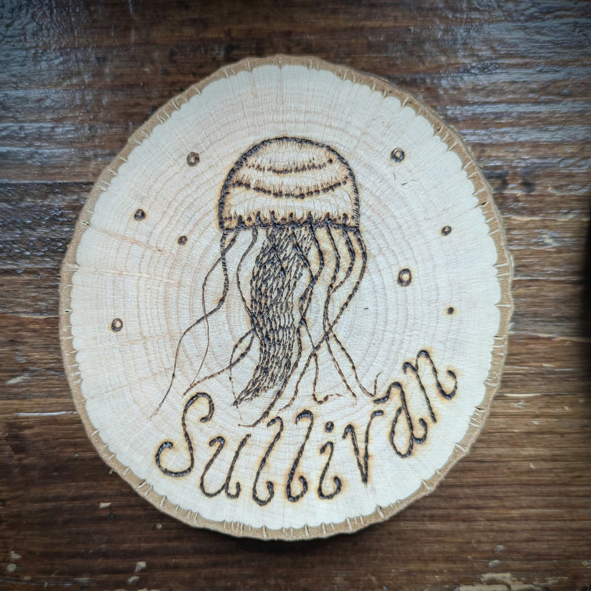 Wooden coaster with a jellyfish design and 'Sullivan' engraving on a wooden surface
